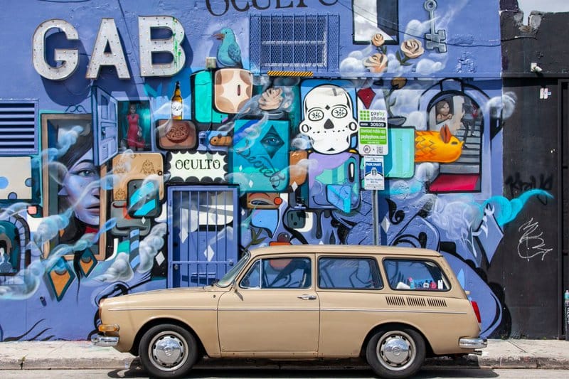 A vintage car parked in front of a creative wall