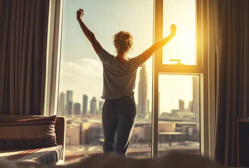 Mulher feliz se alonga e abre cortinas na janela pela manhã