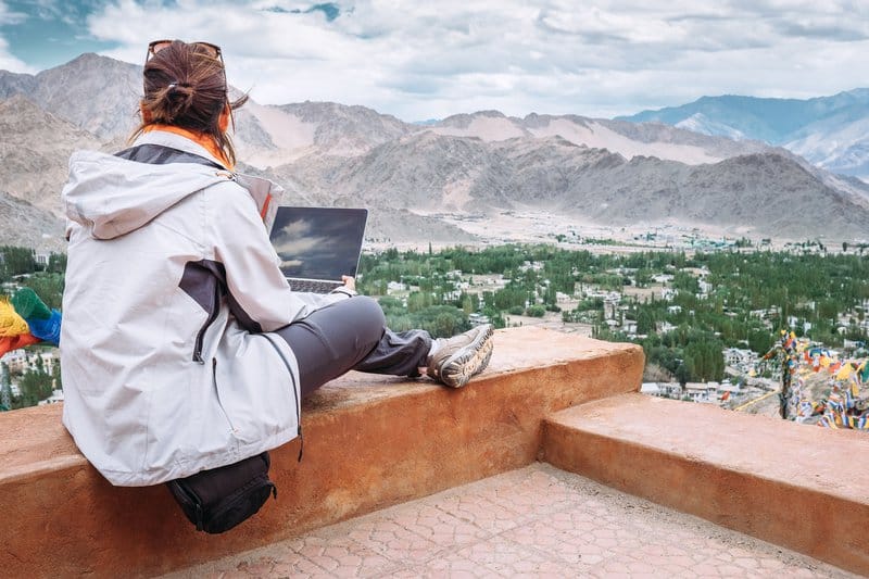 Viajero con computadora portátil se sienta en el mirador superior en el valle de la montaña