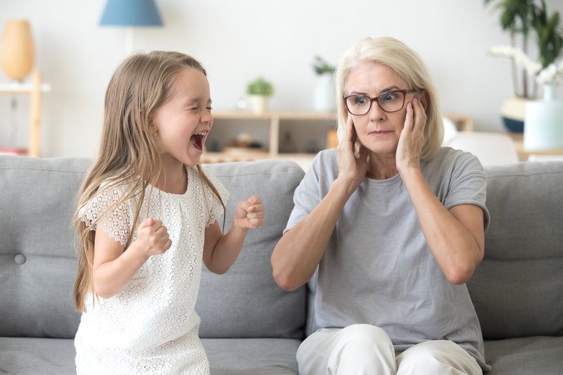 Shocked grandma closing ears not to hear stubborn granddaughter screaming