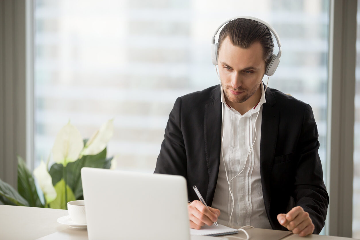 Businessman in headphones taking notes in front of laptop for a remote interview