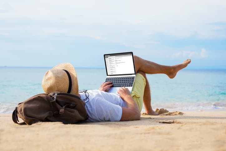 Homem irreconhecível lendo e-mail no laptop enquanto relaxa na praia