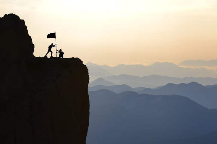 imagem de dois homens na montanha cravando uma bandeira