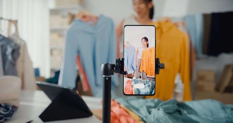 Asian woman live-streamed ecommerce sell clothes at home, beautiful girl using the smartphone and tablet for recording video.