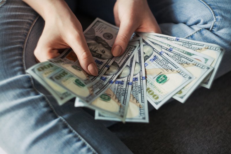 Reaching 8 figures: Someone holding 100 U.S. dollar banknotes